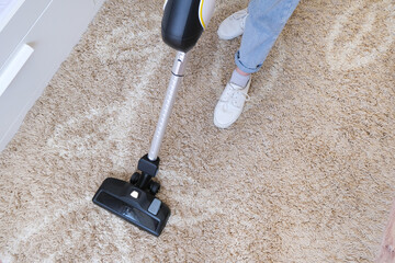 cordless vacuum cleaner is used to clean the carpet in the room. Housework with a new handheld vacuum cleaner. - obrazy, fototapety, plakaty