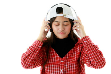 Dreamy Asian female in cool outfit listening to music in headphones and enjoying songs with closed eyes on white background in studio