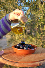 woman's hand pouring olive oil from a jug over a bowl of black olives
