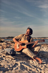 Hippy guitarist with camper house enjoying playing guitar on a sea coast in summertime.