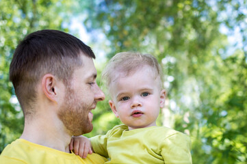 Dad is holding his son in his arms in the park. Father's day