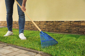 Young man raking grass sods at backyard, closeup - obrazy, fototapety, plakaty