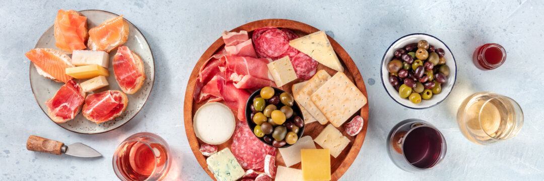 Italian antipasti or Spanish tapas panorama. Gourmet cold meat and cheese platter on a table, shot from the top with wine. A variety of appetizers. Mediterranean party with drinks