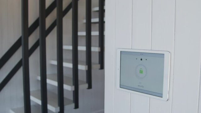 Slowmo shot of young woman entering house while wall-mounted tablet turning smart home security system off
