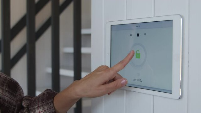 Slowmo close up shot of young woman walking up to wall-mounted tablet and turning smart home security system off