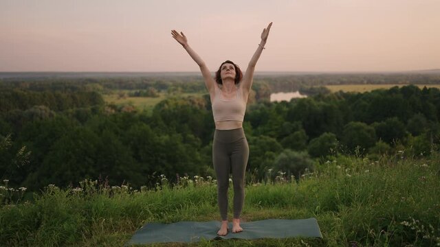 Young woman preforms yoga in mountains in morning light. Woman performs yoga moves on mountain summit. Serenity and yoga practicing at mountain range,meditation