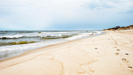 Fototapeta na wymiar Sea waves and footprints on the sand on the beach and overcast sky