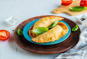 Chebureks or pasties, traditional deep-fried meat pies on a blue plate on a light concrete background.