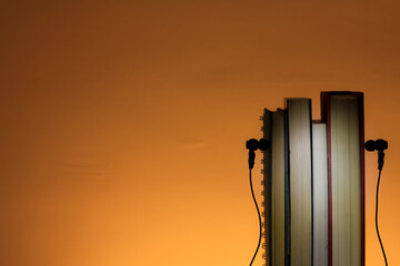 Abstract Book with earphone. E book, Audio Book. Shoot in orange color background. With a grow...