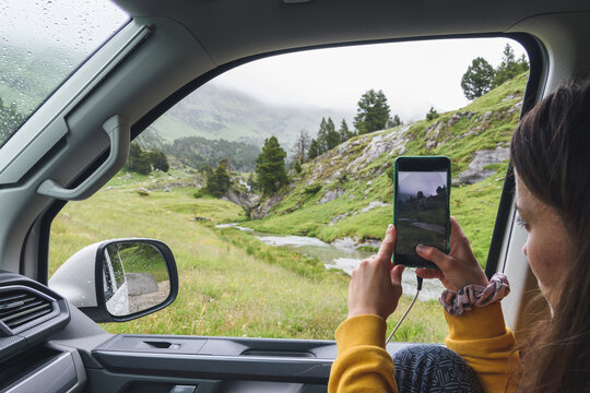 girl taking a picture of a landscape from the window of a camper van