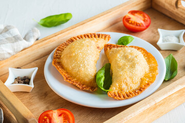 Chebureks or pasties, traditional deep-fried meat pies on a wooden tray on a light concrete background.