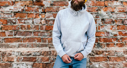City portrait of handsome hipster guy with beard wearing gray blank hoodie or sweatshirt and hat...