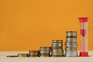 The red hourglass and stacks of coins are in one row in Ascending order. Financial growth concept