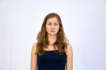 The woman thought for a moment and looks with surprise. A beautiful Caucasian woman stands on a white background in a blue sweater with loose hair. The woman shows emotions.