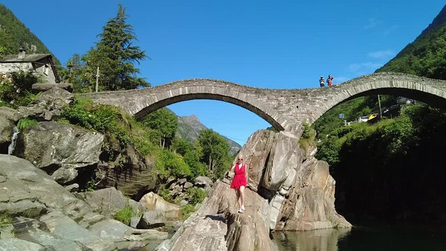 SLOW MOTION: Woman running under Roman stone bridge: Ponte dei Salti over Verzasca River. Verzasca valley by Lavertezzo. Famous landmark for riverside leisure and high diving in Ticino, Switzerland.