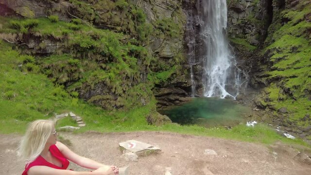Woman sitting by the Froda waterfall or Sonogno waterfall over the Riale Carded river in Sonogno town of Switzerland. Riale Carded river in Verzasca valley in Ticino region.