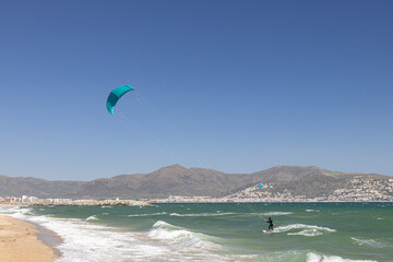 A kiteboarder is pulled across water by a power kite in strong onshore winds in Empuriabrava, Costa Brava, province of Girona, Catalonia, Spain. Kiteboarding, kitesurfing, extreme sport.
