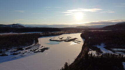 bright sunset sunlight over deep norwegian forest and frozen river landscape aerial shot, maalselv county in northern Norway