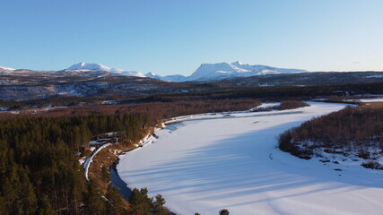 bright sunset sunlight over deep norwegian forest and frozen river landscape aerial shot, maalselv county in northern Norway