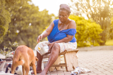landscape image of black woman feeding a canine in african home