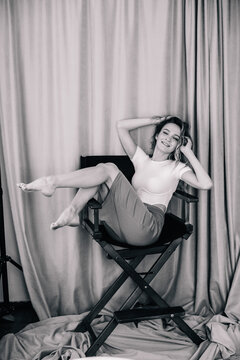 Young, slender girl in bodysuit sits on the director's chair in the photo studio