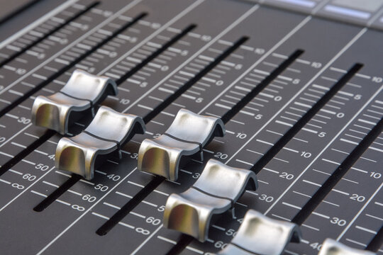 Close up of the silver faders of an audio mixer with gray background