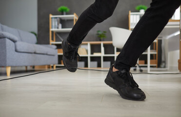Fototapeta na wymiar Person in uncomfortable sneakers trips over electric cord at home. Closeup male office worker in black shoes stumbles on power cable. Close up shot feet stepping on floor. Injury and accident concept