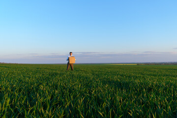 Fototapeta na wymiar a businessman holds a cardboard box and poses on a green grass field - business concept