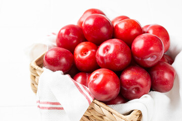 Chinese or Korean red plum in a basket on a white table closeup. Summer harvest