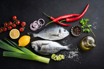 Uncooked dorado fish with spices and vegetables on black slate background, table top view. Cooking healthy food, web banner flat lay design