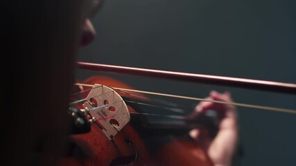 On string musical instrument violin, a woman musician plays with bow, a close-up in darkness studio. Concept of classic music.