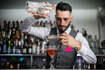 Bartender with sieve pouring drink into glass