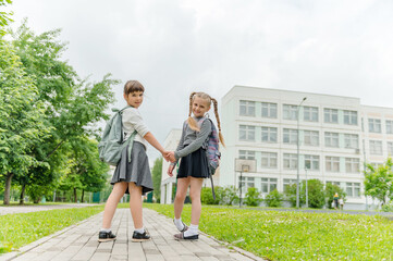 two cute happy girls schoolgirls with backpacks are playing near the school. High quality photo