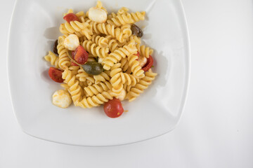 Piatto di pasta con pomodori, mozzarella, olive e capperi su sfondo bianco