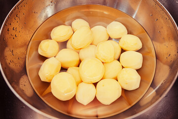 Raw, peeled potatoes submerged in water  in chrome bowl in the sink