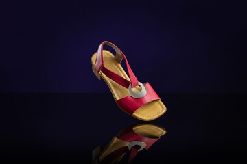 Single red leather women’s sandal on dark blue background. Product photography and shopping...