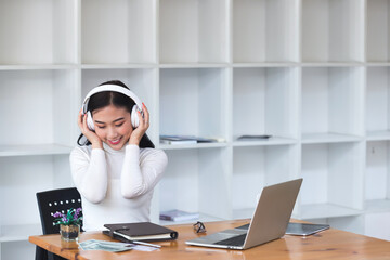 Asian woman wearing headphones listening to music on her laptop and rocking to the rhythm of the music. Relaxing time.