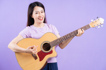 Young Asian woman playing guitar on purple background