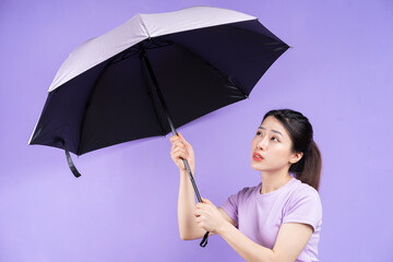 Young Asian woman holding umbrella on purple background