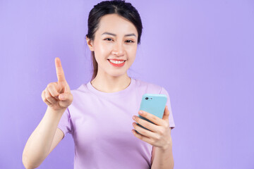 Young Asian woman using smartphone on purple background