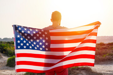 Rear view of man holding waving USA American flag against sunset sky outdoor. Independence day of...