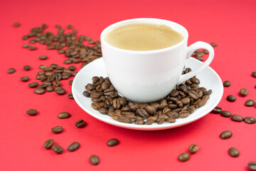 A cup of creamy coffee with roasted coffee beans, red background and copy space