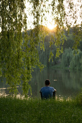 Fototapeta premium young guy alone with thoughts on the lake. Concept: sunset, tranquility