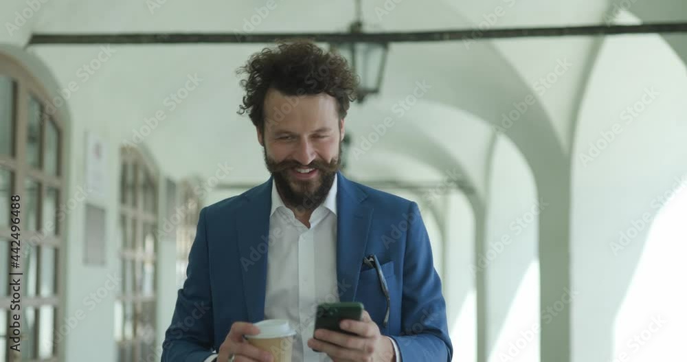 Sticker happy unshaved fashion model drinking coffee, holding phone and reading emails, laughing and walking