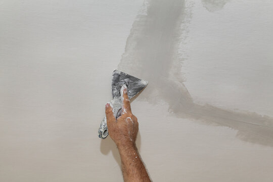 Worker fixing cracks on ceiling or wall, spreading plaster using trowel