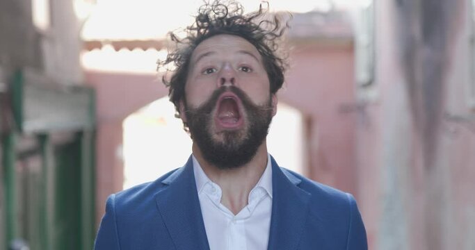 young casual man moving head, having a seizure, being angry and screaming, suddenly getting happy in front of medieval town outdoor