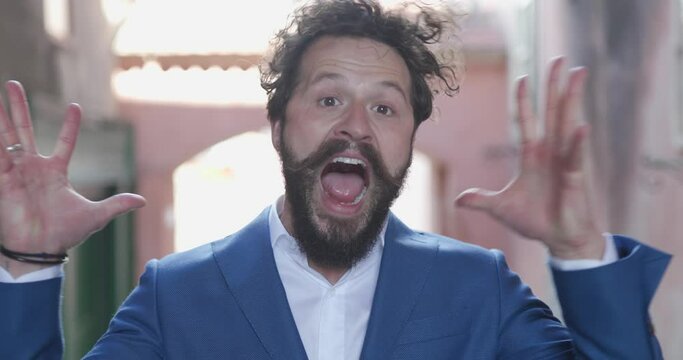 curly hair fashion model with long moustache being angry, screaming and shouting, making hand gestures and fixing hair in medieval city outdoor