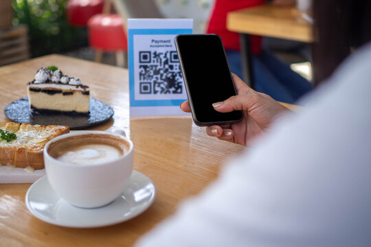 A woman scans the QR code to pay for the food after receiving the order. New-normal to Cashless payment format in cafe or restaurant