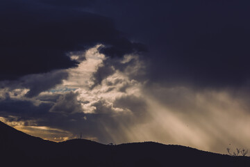 thick stormy clouds over the mountains with intense sun rays peaking through and contrasty light