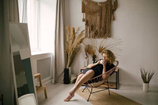 Young woman drinking tea or coffee in a cozy room with bohemian interior.